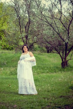 Ormanda beyaz elbiseli hamile kadın.