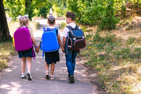Three elementary school students with backpacks walking along the sidewalk.
