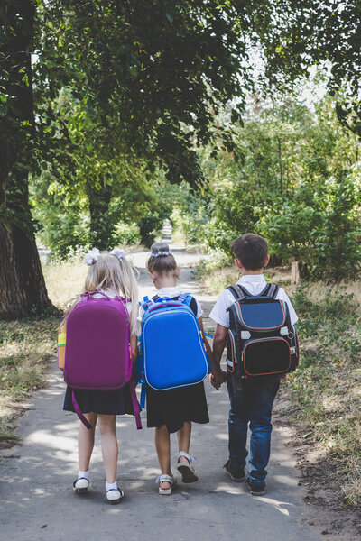 Three elementary school students with backpacks walking along the sidewalk.
