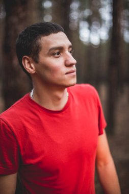 Kırmızı tişört bir çam ormanı içinde genç bir adam.