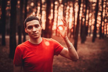 Kırmızı tişört bir çam ormanı içinde genç bir adam.