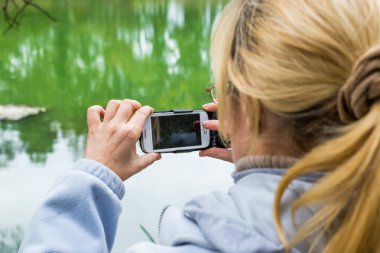 Güzel bir manzara fotoğrafını bir telefonu kullanarak sarışın bir kadın lazım.