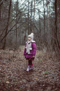 Küçük bir kız bir ormanda yol üzerinde duruyor