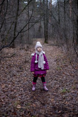 Küçük bir kız bir ormanda yol üzerinde duruyor