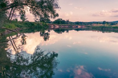 Sakin güzel doğal manzara mavi nehir, yeşil ağaçlar ve su bulutlu gökyüzü ile yansıtan. Büyülü günbatımı kırsal arazide Nehri. Doğal, vahşi manzara.