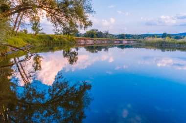 Sakin güzel doğal manzara mavi nehir, yeşil ağaçlar ve su bulutlu gökyüzü ile yansıtan. Büyülü günbatımı kırsal arazide Nehri. Doğal, vahşi manzara.