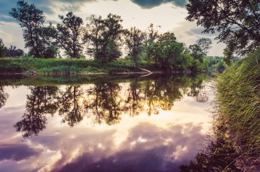 Sakin güzel doğal manzara mavi nehir, yeşil ağaçlar ve su bulutlu gökyüzü ile yansıtan. Büyülü günbatımı kırsal arazide Nehri. Doğal, vahşi manzara.
