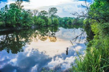 Sakin güzel doğal manzara mavi nehir, yeşil ağaçlar ve su bulutlu gökyüzü ile yansıtan. Büyülü günbatımı kırsal arazide Nehri. Doğal, vahşi manzara.