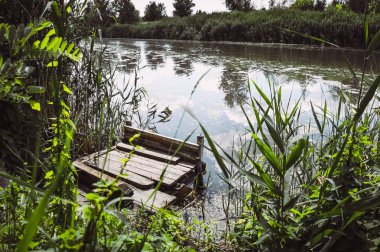 Ahşap platform yaz aylarında nehir üzerinde balıkçılık için. Duckweed, ağaçlar ve gökyüzü su yansıması.