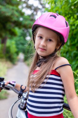 Yaz aylarında bir bisiklet yakınındaki pembe bir kask içinde küçük şirin kız