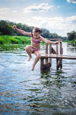Küçük şirin kız dock güzel nehre günbatımında atlama..