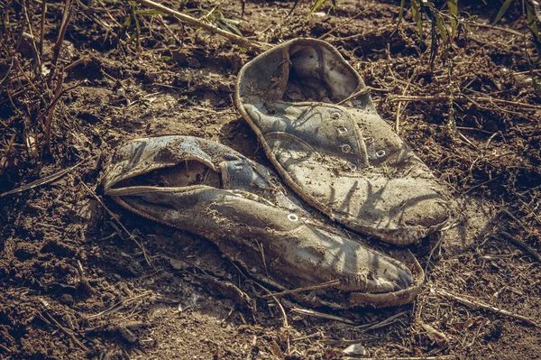 Old dirty grey sneakers abandoned on the ground. Toned, style photo