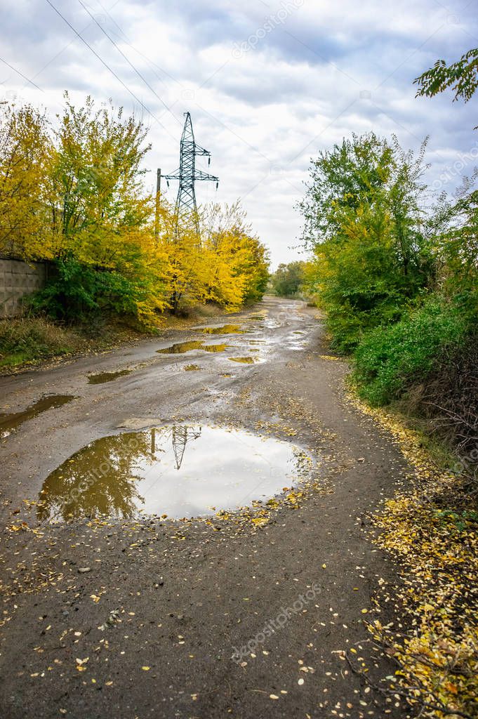 Old road with puddles in the industrial area in autumn