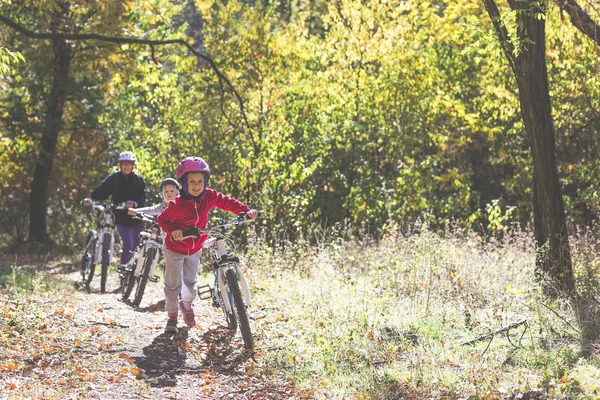 Mother and two daughters with bikes go uphill in the autumn forest