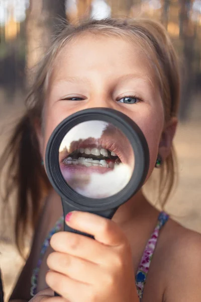 A little girl put a magnifying glass to her mouth to show an ort — Stock Photo, Image