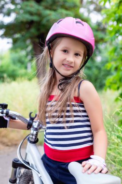 Bir bisiklet yakınındaki pembe bir kask içinde küçük şirin kız