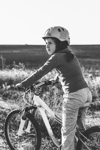 Little girl on a bike wearing a helmet on a dirt road in the fie — Stock Photo, Image