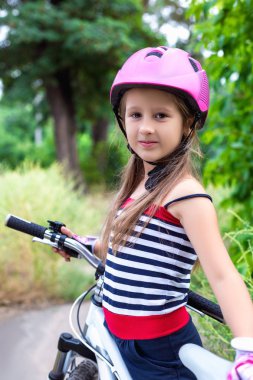 Bir bisiklet yakınındaki pembe bir kask içinde küçük şirin kız