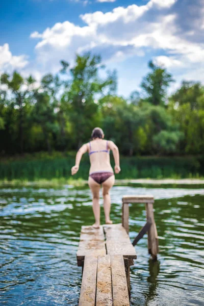 En vacker kvinna hoppar i vattnet från en brygga. — Stockfoto