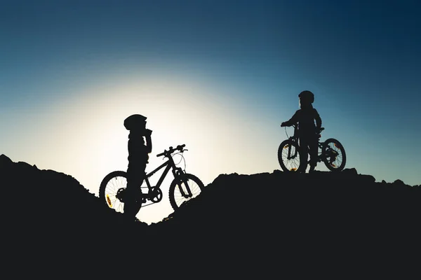 Silhouet van twee kleine meisjes met fietsen bij zonsondergang — Stockfoto