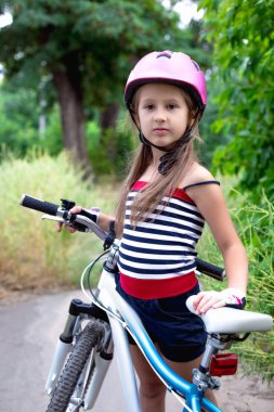 Bir bisiklet yakınındaki pembe bir kask içinde küçük şirin kız