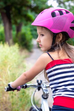 Bir bisiklet yakınındaki pembe bir kask içinde küçük şirin kız