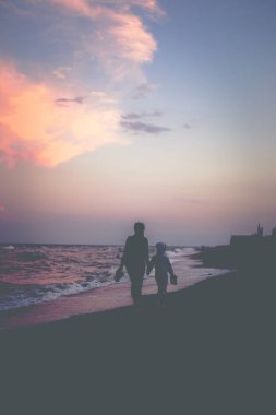 Anne ve kızı gün batımında plaj boyunca yürümek