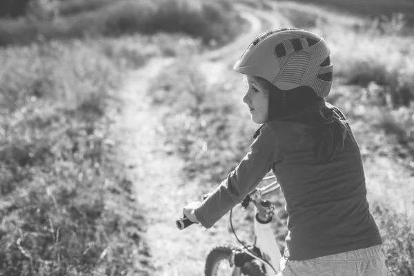 Niña en una bicicleta con un casco en un camino de tierra en el fie —  Fotos de Stock