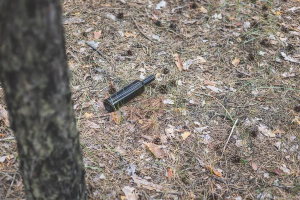 Barna üvegpalack a földön egy fenyőerdőben. — Stock Fotó