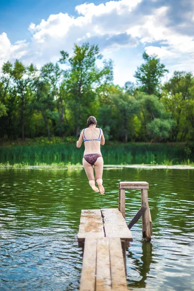 En vacker kvinna hoppar i vattnet från en brygga. — Stockfoto