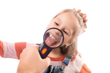 Beyaz arka planda ortodontik bir aletle büyüteçle küçük tatlı bir kızın portresi..