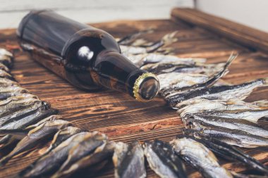 Ahşap bir arka planda ipte küçük kuru balık ve kahverengi bira şişesi. Stüdyo fotoğrafı.