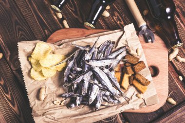 Kahverengi cam bira şişeleri ve kurutulmuş balık, cips, fındık ve tahta arka planda kraker. Stüdyo fotoğrafı.