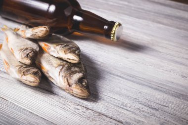 Beyaz ahşap arka planda kurumuş levrek ve kahverengi cam bira şişesi. Stüdyo fotoğrafı.