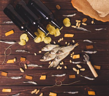 Kurutulmuş balık, levrek, kasvetli cips, kraker, fındık ve ahşap zemin üzerinde üç kahverengi cam bira şişesi. Stüdyo fotoğrafı.