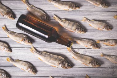 Beyaz ahşap arka planda kurumuş levrek ve kahverengi cam bira şişesi. Stüdyo fotoğrafı.