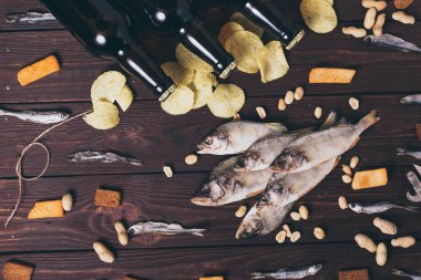 Kurutulmuş balık, levrek, kasvetli cips, kraker, fındık ve ahşap zemin üzerinde üç kahverengi cam bira şişesi. Stüdyo fotoğrafı.