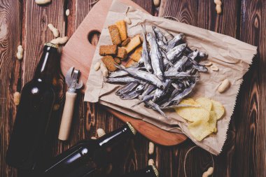 Kahverengi cam bira şişeleri ve kurutulmuş balık, cips, fındık ve tahta arka planda kraker. Stüdyo fotoğrafı.