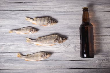 Beyaz ahşap arka planda kurumuş levrek ve kahverengi cam bira şişesi. Stüdyo fotoğrafı.