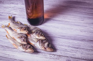 Beyaz ahşap arka planda kurumuş levrek ve kahverengi cam bira şişesi. Stüdyo fotoğrafı.