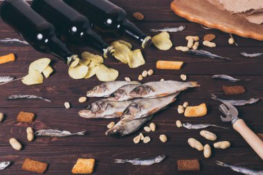 Kurutulmuş balık, levrek, kasvetli cips, kraker, fındık ve ahşap zemin üzerinde üç kahverengi cam bira şişesi. Stüdyo fotoğrafı.