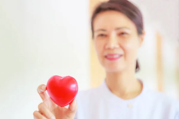 Red heart held by smiling female nurse\'s hand, representing giving effort high quality service mind to patient. Professional, Specialist in white uniform concept