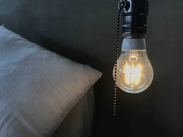 The warm orange glowing incandescent light bulb on the head of the white wooden bed. Loft Interior Design, comfortable and relaxing furniture, pop up idea at wake up concept