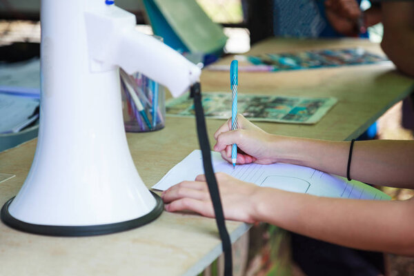 woman guide hand writing on document paper next to white megaphone on table, preparing permits for group of tourists trips. Tourism Business, Occupation, Official Documentation and Permission concept