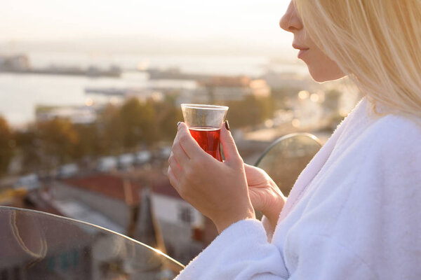A girl in a bathrobe with a cup of Turkish tea at sunrise on the terrace of a house in Istanbul