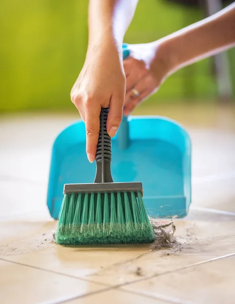 A woman sweeps up dust and dirt from the floor while cleaning the house