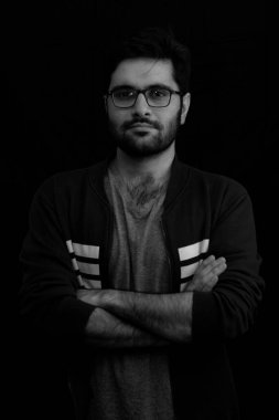 Siyah ve beyaz bir görüntü, gülümseyen genç bir adamın karanlık odada duruşu.