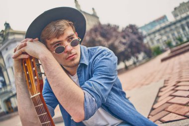 Gitar çalan genç bir adam. Şapkalı şık hippi adam eğleniyor.