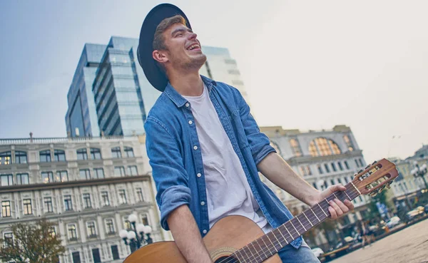 Young man playing the guitar. Stylish hipster guy with hat enjoy