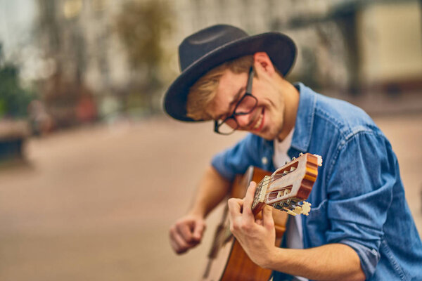 Молодой человек играет на гитаре. Стильный парень-хипстер в шляпе
